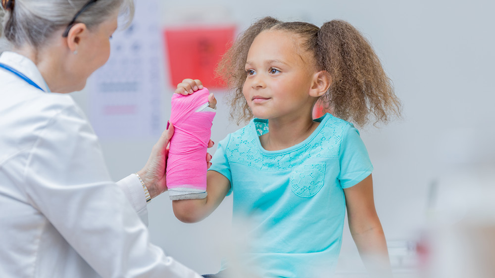 doctor examining young Black girl's injured arm in pink cast
