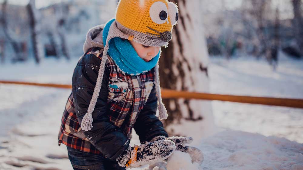 child building snowman outside in winter