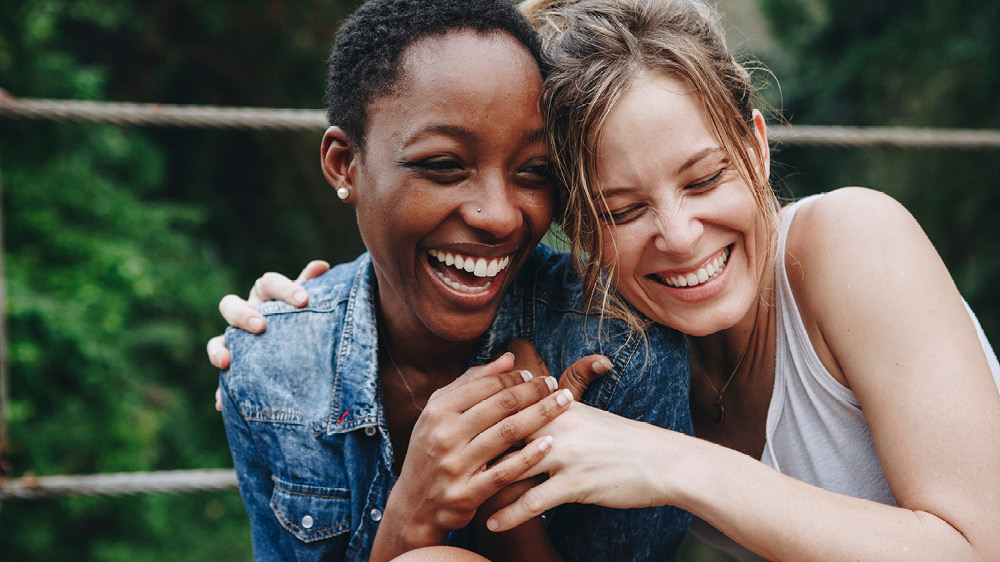 two women smiling and hugging outside